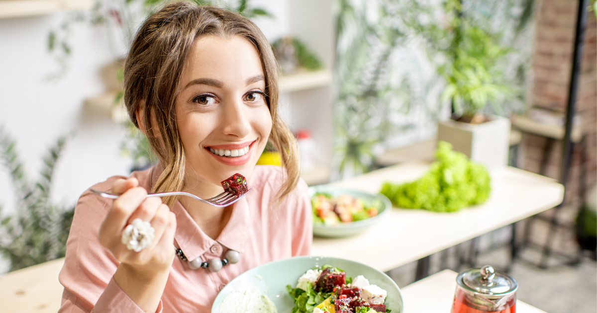 Smiling woman enjoying a fresh, healthy salad in a bright, plant-filled setting